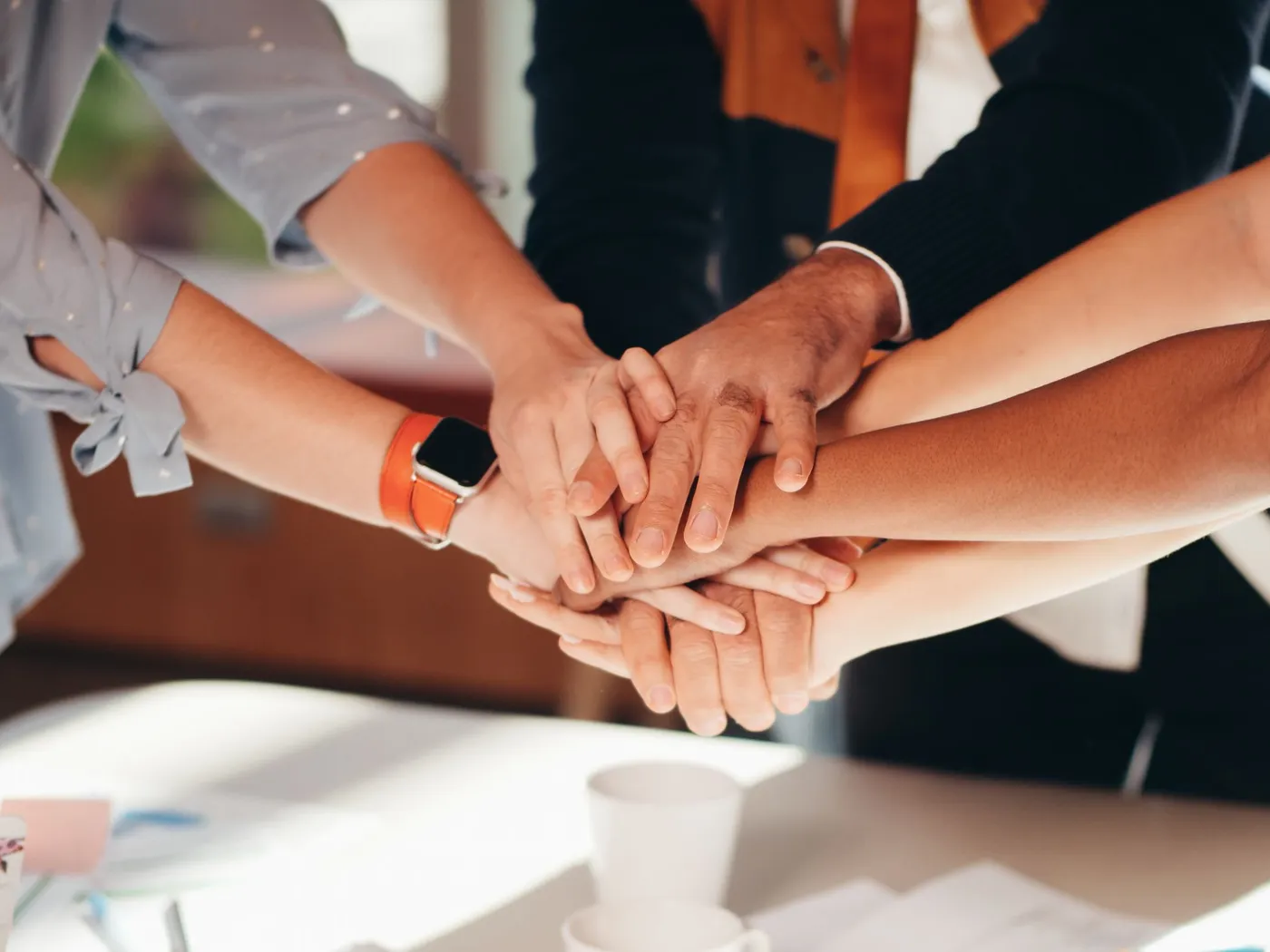 Un equipo junta las manos, una sobre otra, sobre una mesa de trabajo.